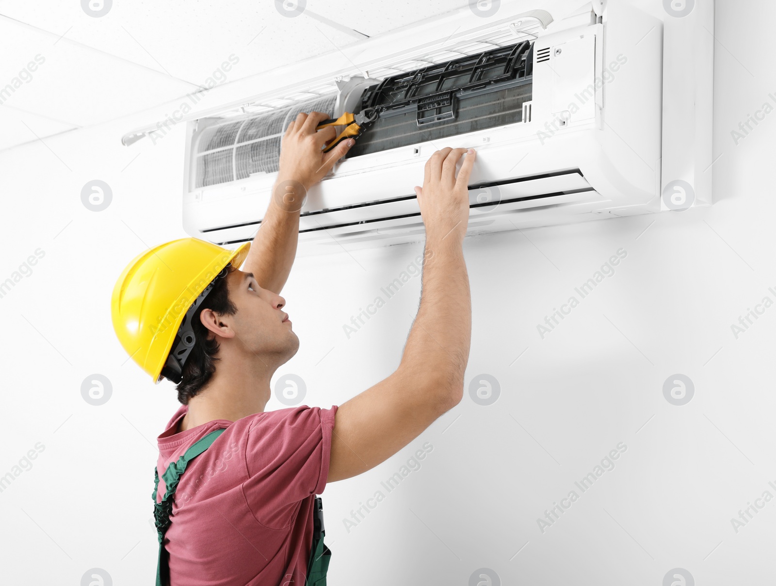 Photo of Male technician checking and repairing air conditioner indoors