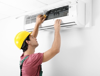 Photo of Male technician checking and repairing air conditioner indoors