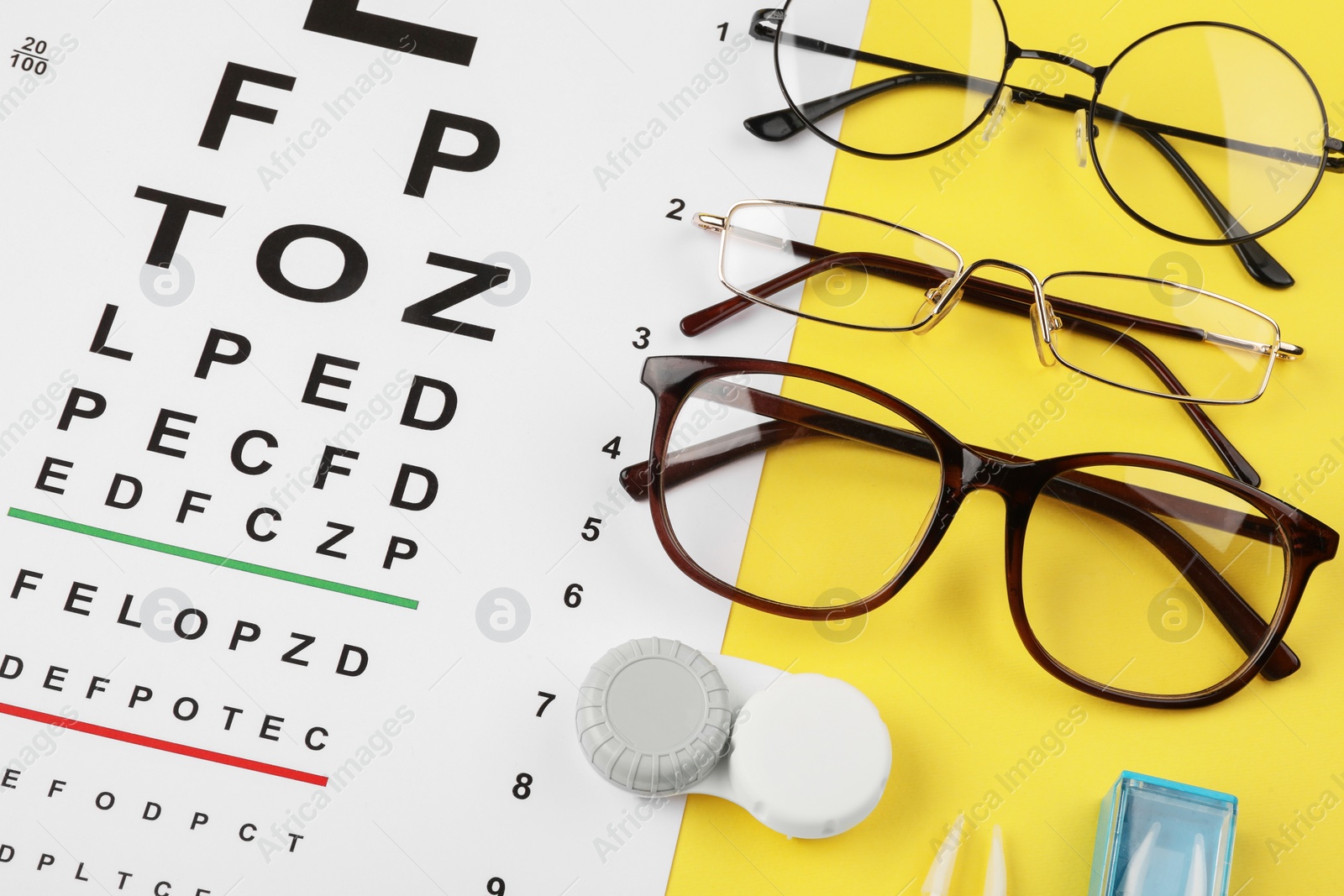 Photo of Vision test chart, glasses and lenses on yellow background, flat lay