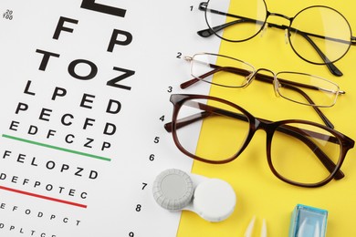 Photo of Vision test chart, glasses and lenses on yellow background, flat lay
