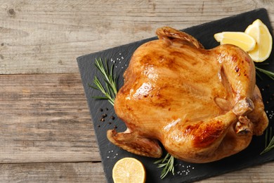 Photo of Tasty roasted chicken with spices and lemon on wooden table, top view