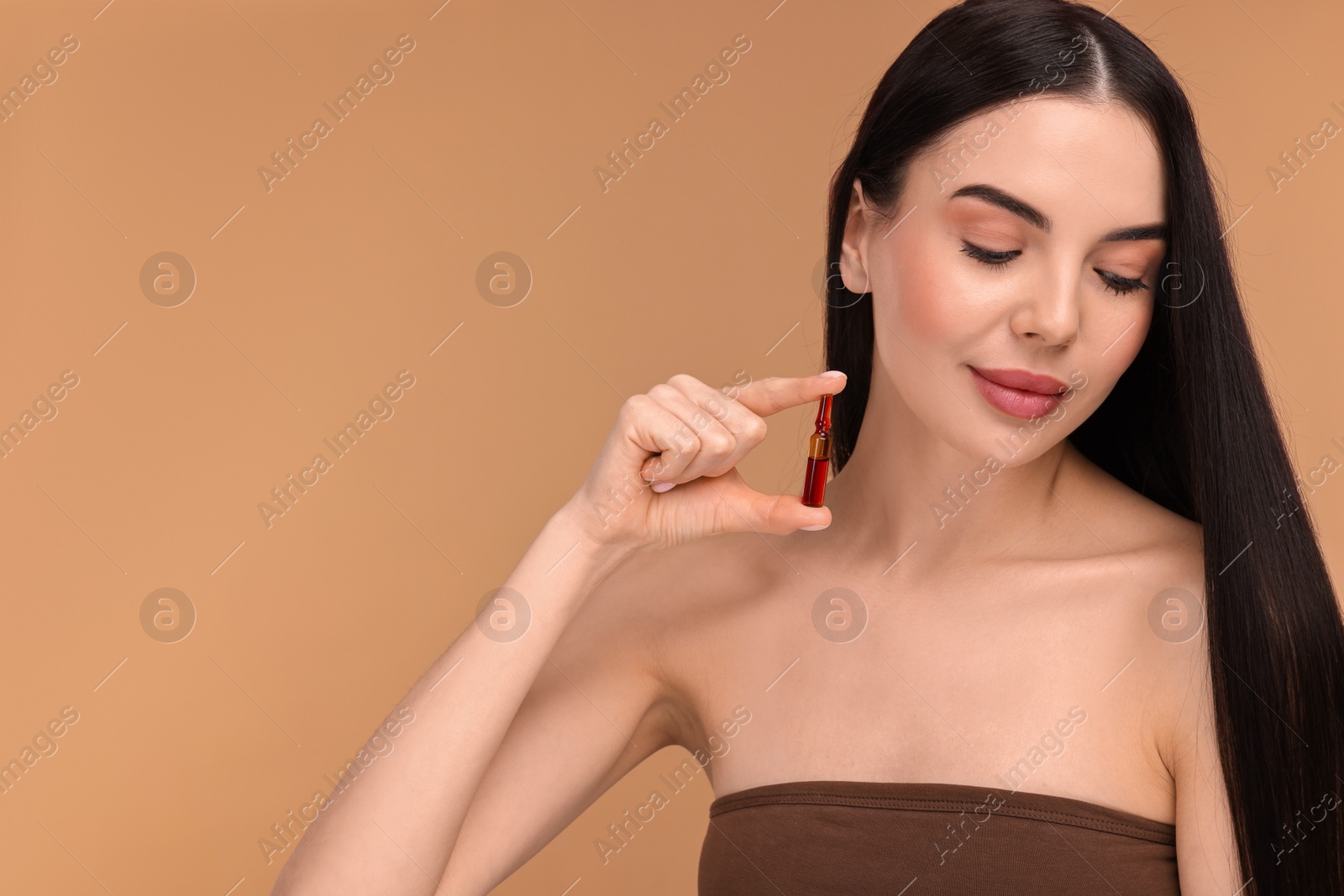 Photo of Beautiful young woman holding skincare ampoule on beige background. Space for text