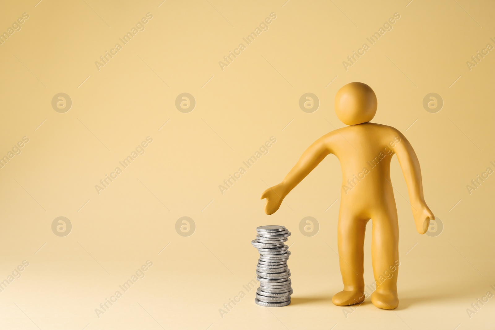 Photo of Human figure made of yellow plasticine with stacked coins on beige background. Space for text