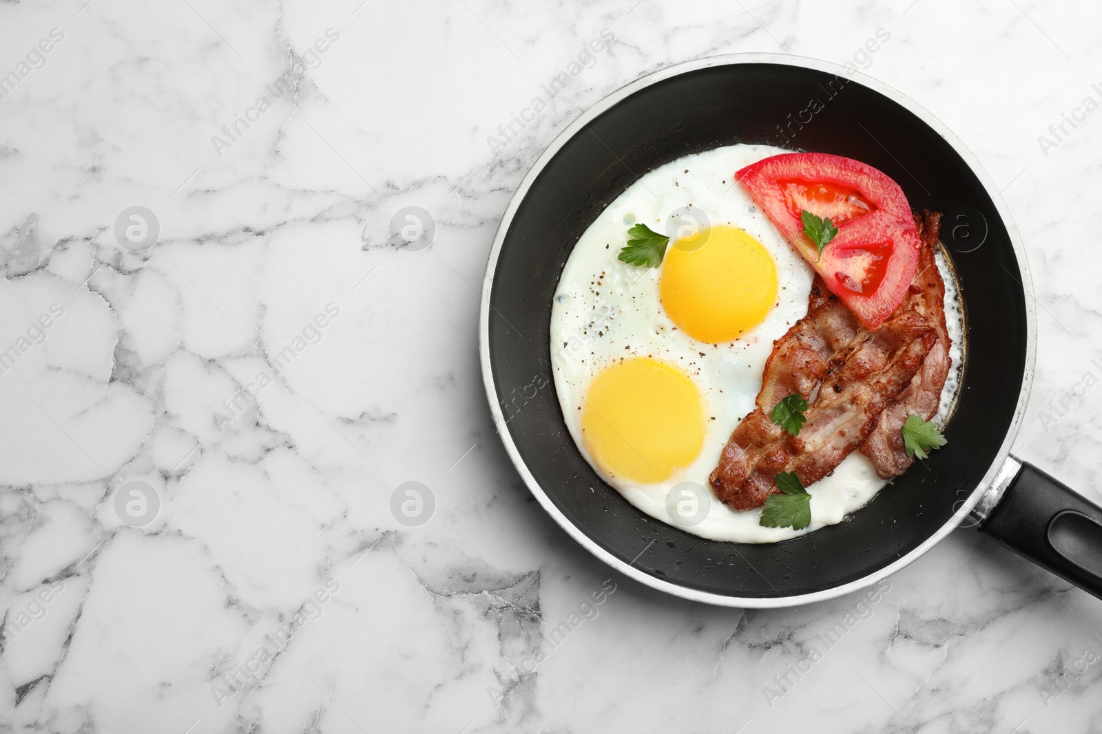 Photo of Fried sunny side up eggs with tomato and bacon in pan on marble background, top view. Space for text