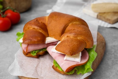 Photo of Tasty crescent roll with brie, ham and lettuce on grey table, closeup