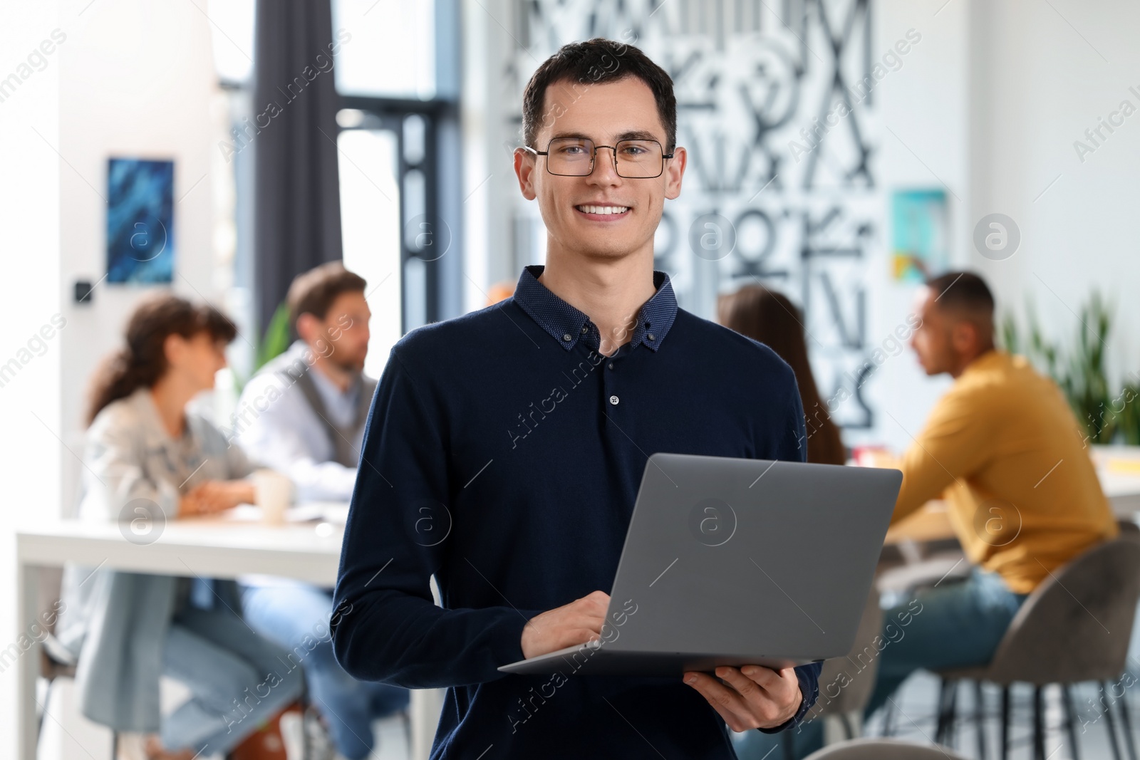 Photo of Team of employees working together in office. Happy man with laptop indoors