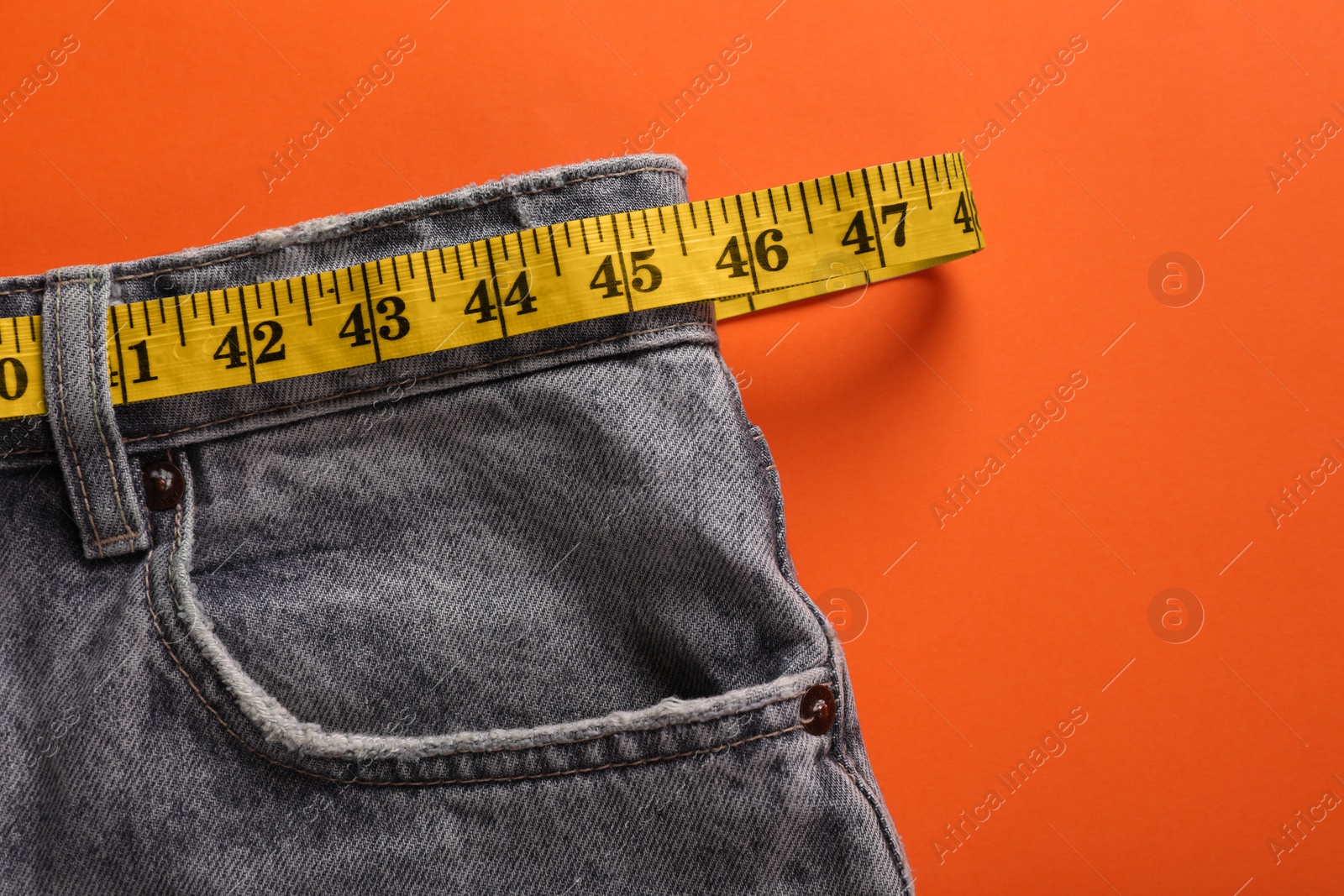 Photo of Jeans and measuring tape on orange background, top view with space for text. Weight loss concept