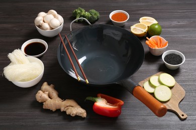 Photo of Empty iron wok and chopsticks surrounded by ingredients on dark grey wooden table