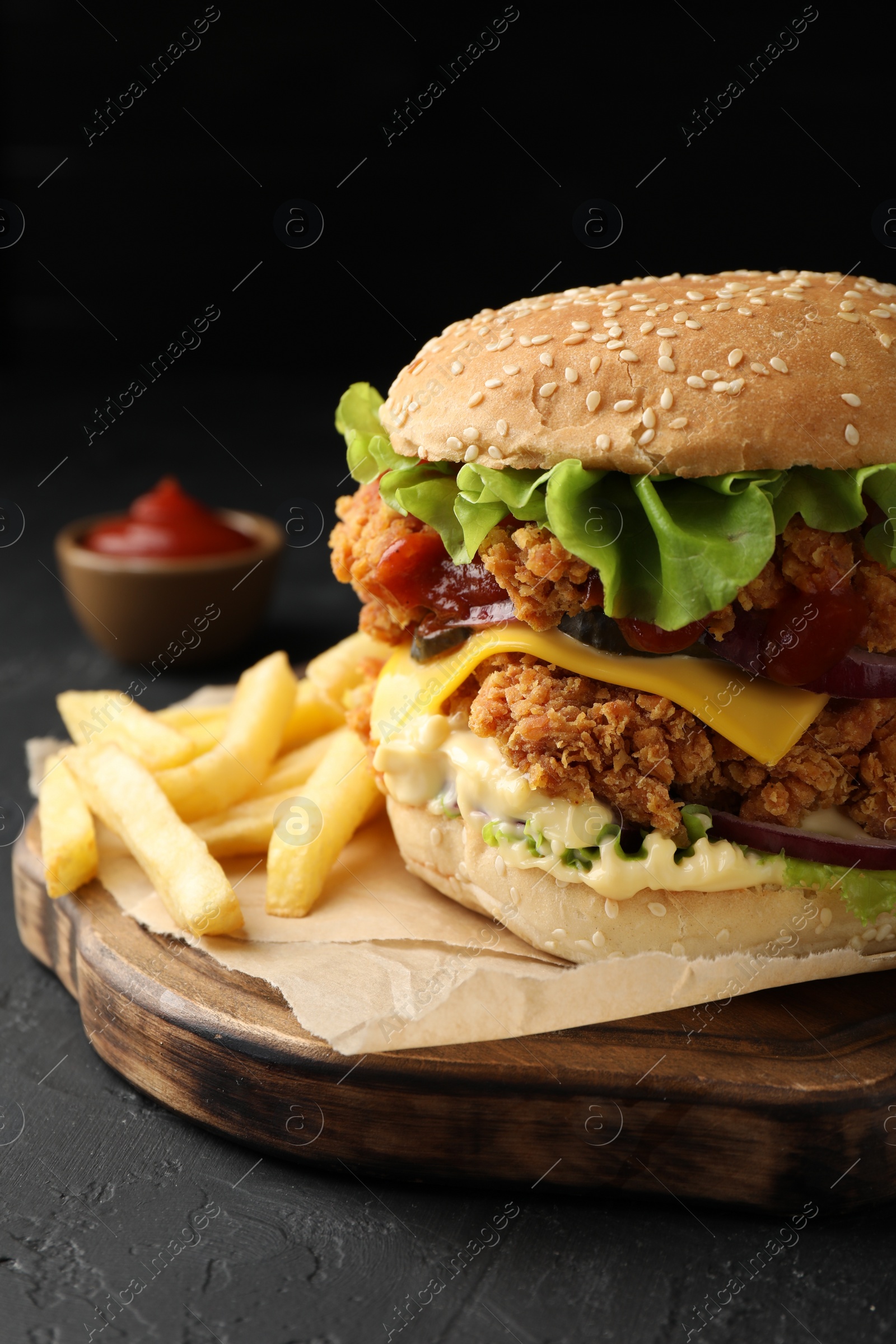 Photo of Delicious burger with crispy chicken patty, french fries and sauce on black table, closeup