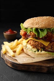 Photo of Delicious burger with crispy chicken patty, french fries and sauce on black table, closeup