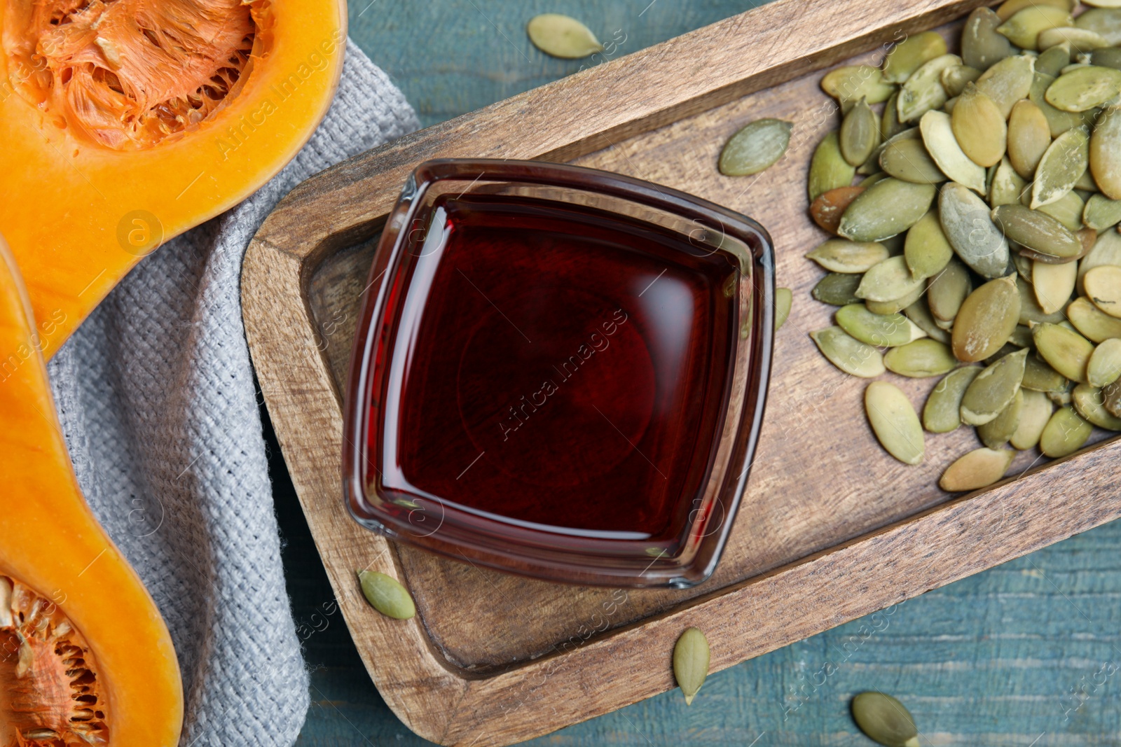 Photo of Glass bowl of oil and pumpkin seeds on wooden table, flat lay