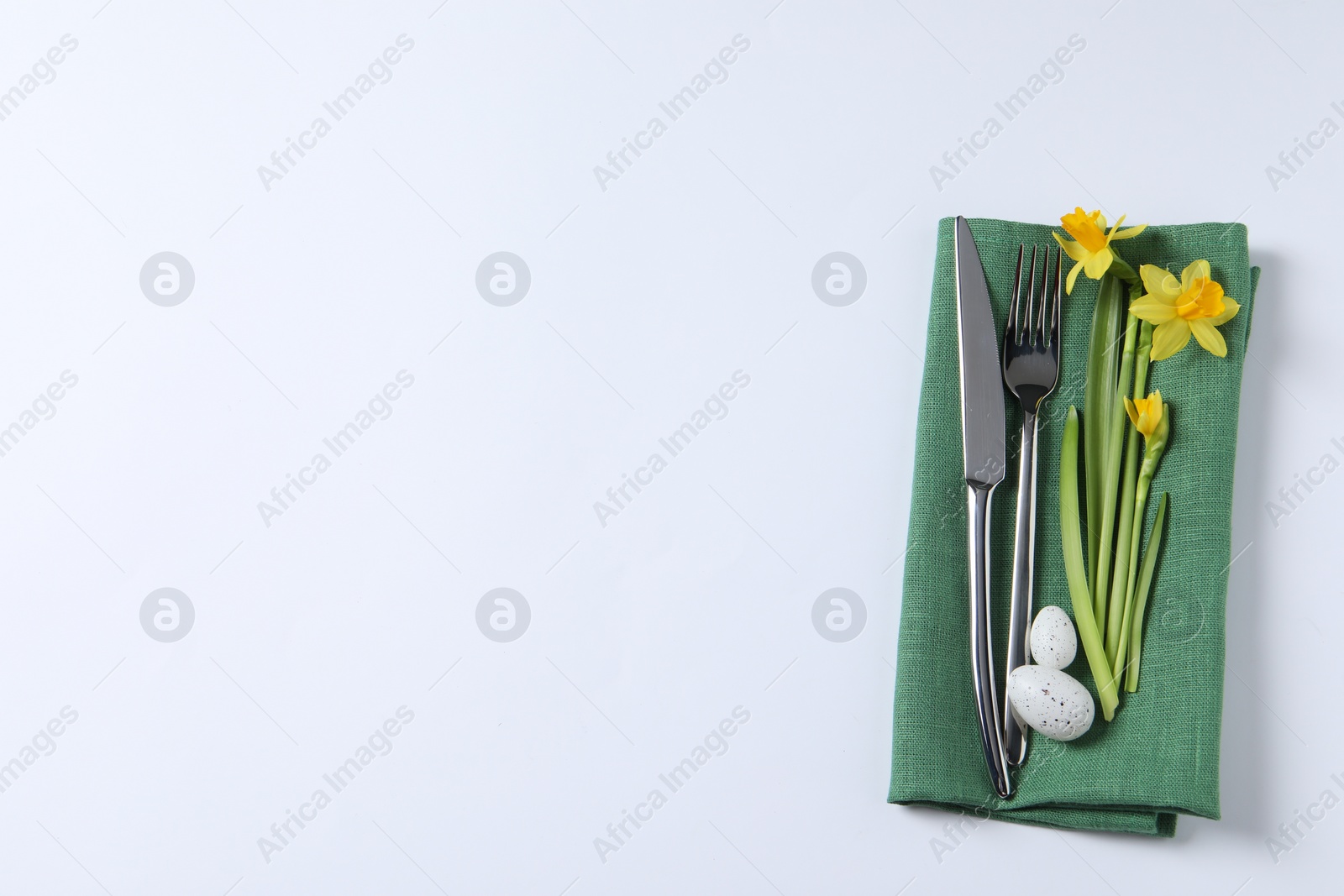 Photo of Cutlery set, Easter eggs and narcissuses on white background, top view with space for text. Festive table setting