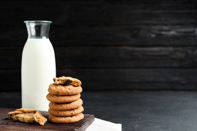 Photo of Delicious cookies with raisins and milk on black table. Space for text