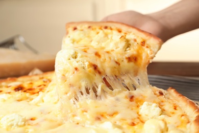 Photo of Woman holding slice of delicious hot pizza over table, closeup