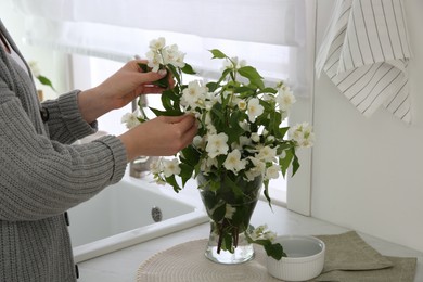 Photo of Woman making bouquet with beautiful jasmine flowers in kitchen, closeup