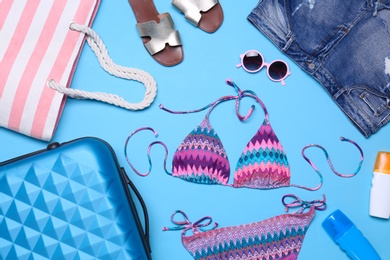 Photo of Suitcase and beach objects on blue background, flat lay