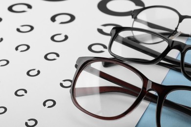 Vision test chart and different glasses on table, closeup