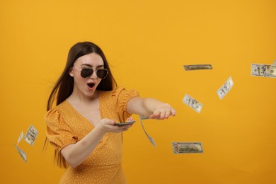 Happy woman throwing money on orange background