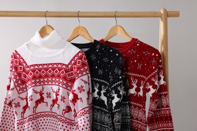 Different Christmas sweaters hanging on rack against light background