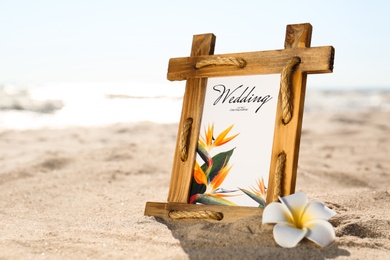 Photo of Beautiful wedding invitation and flower on sandy beach, closeup. Space for text