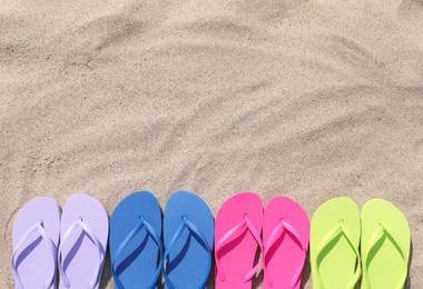 Photo of Many stylish colorful flip flops on sand outdoors, flat lay. Space for text