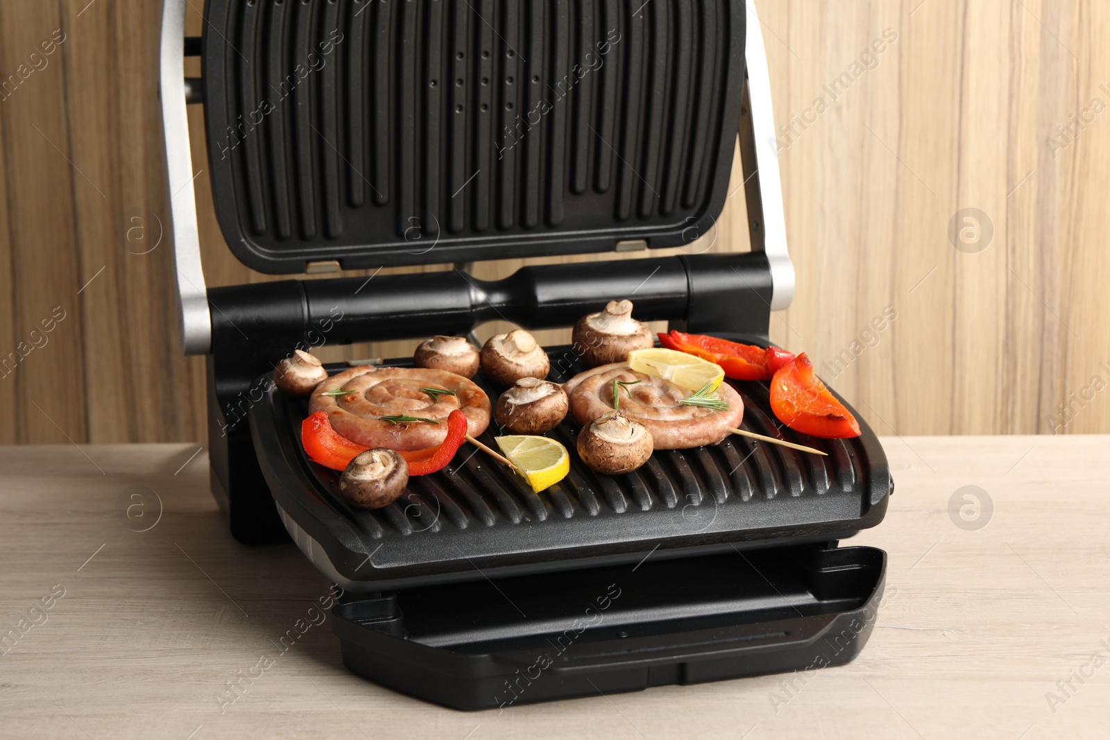 Photo of Electric grill with homemade sausages, mushrooms and bell pepper on wooden table