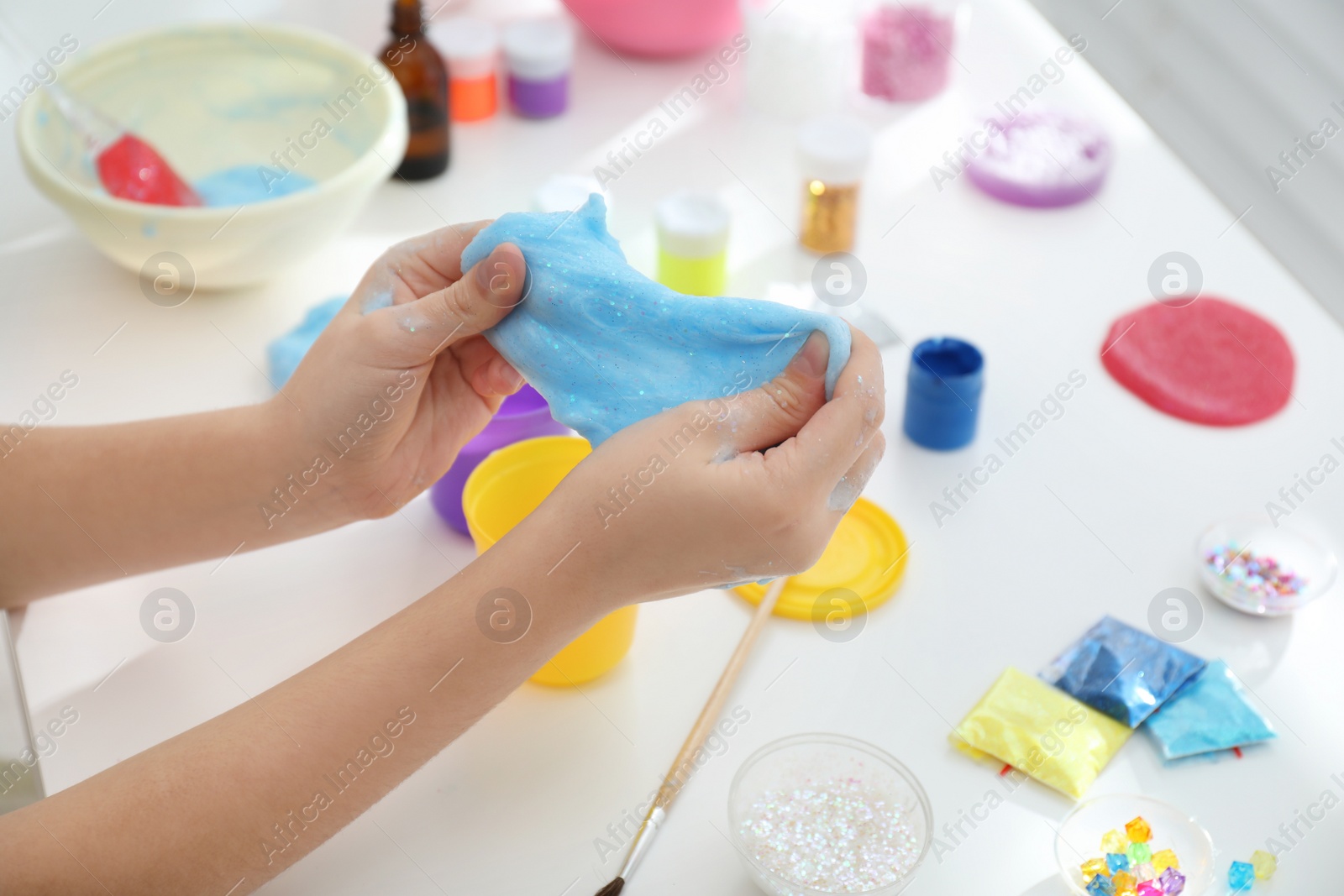 Photo of Little girl making DIY slime toy at table, closeup