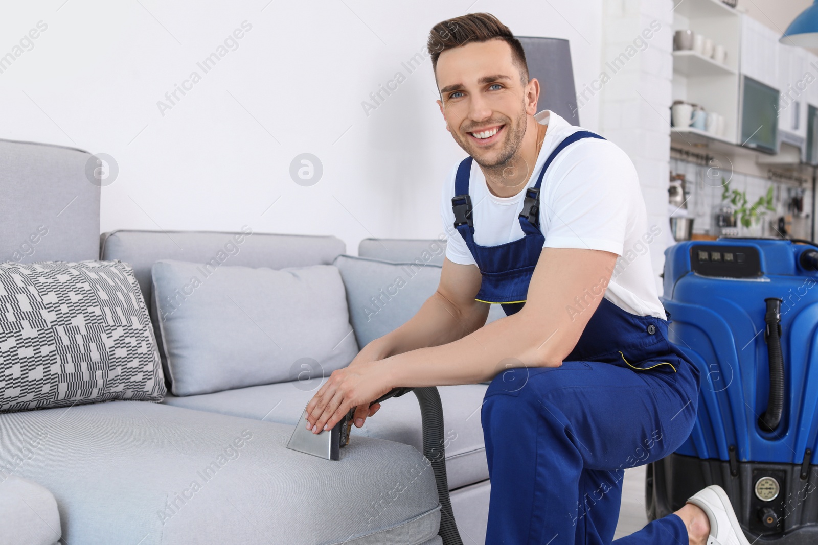 Photo of Male worker removing dirt from sofa with professional vacuum cleaner indoors