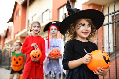 Photo of Cute little girl with pumpkin candy bucket wearing Halloween costume outdoors