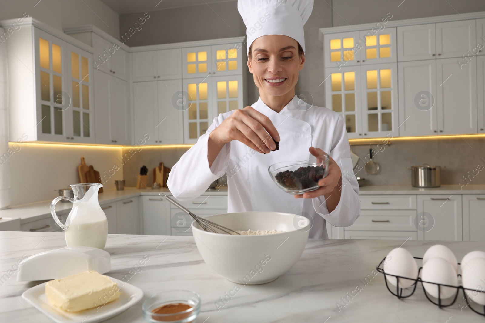 Photo of Professional chef adding raisins into dough at white marble table in kitchen