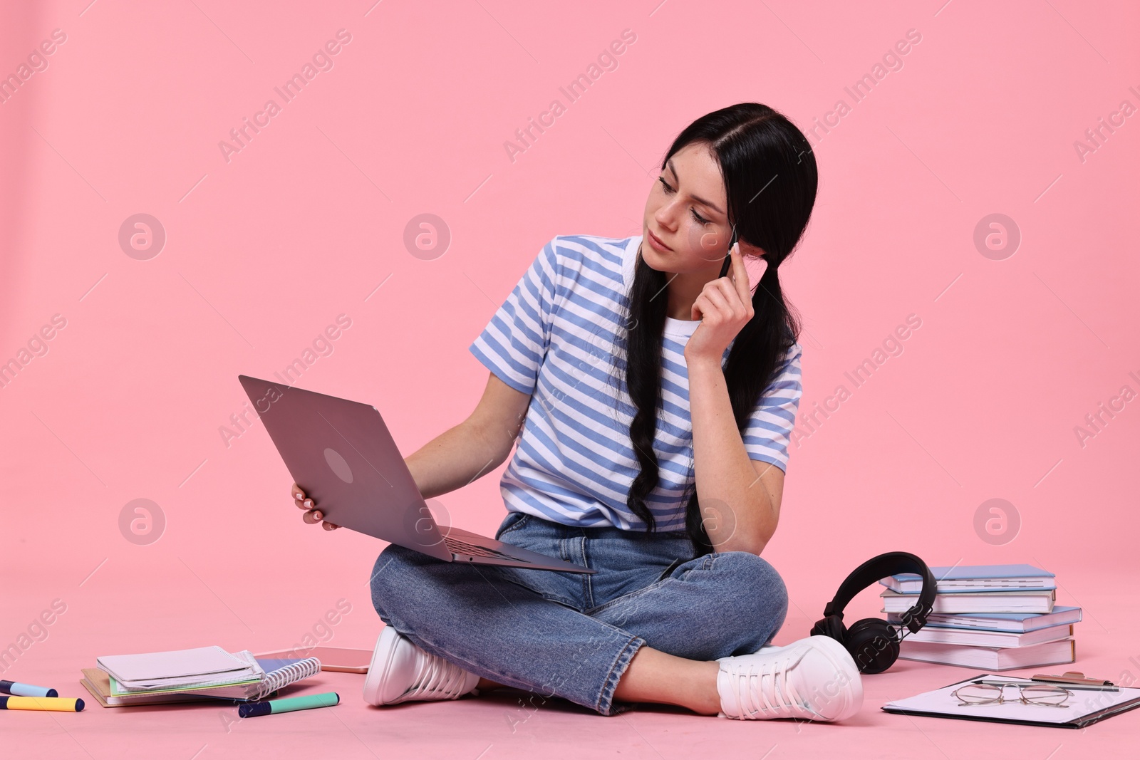 Photo of Student with laptop sitting among books and stationery on pink background