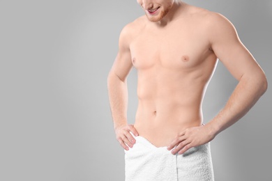 Photo of Young man with slim body in towel on grey background, closeup. Space for text