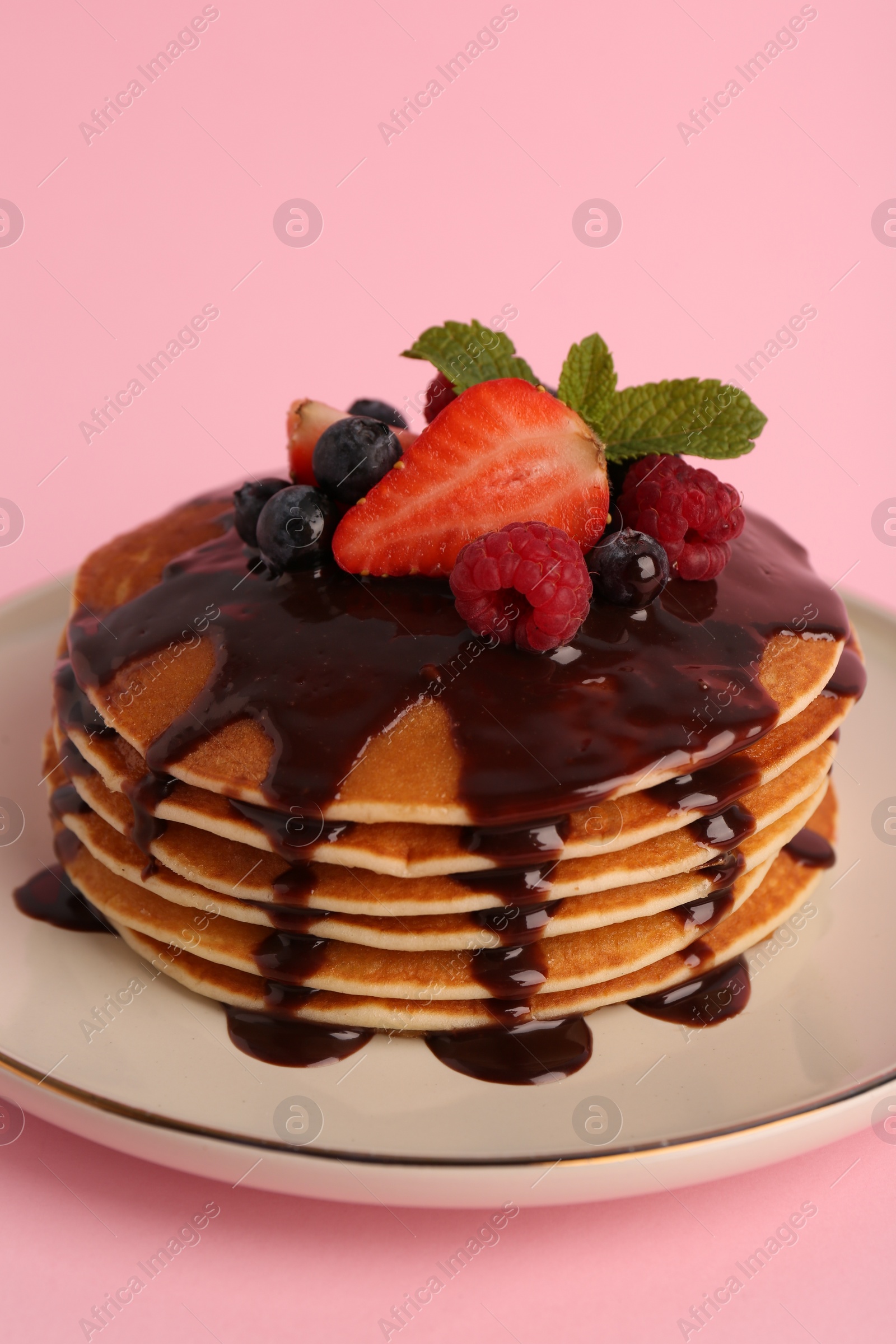 Photo of Stack of tasty pancakes with fresh berries, chocolate sauce and mint on pink background, closeup