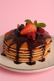 Stack of tasty pancakes with fresh berries, chocolate sauce and mint on pink background, closeup