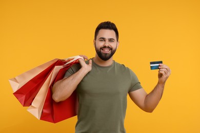 Photo of Smiling man with many paper shopping bags and credit card on orange background