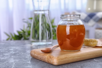 Photo of Glass jar with sweet honey and spoon on wooden board