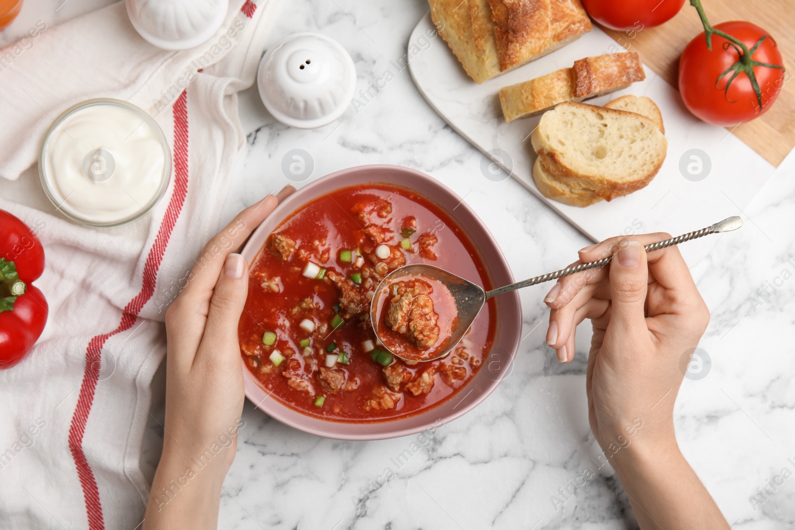 Photo of Woman with bowl of delicious stuffed pepper soup at white marble table, top view