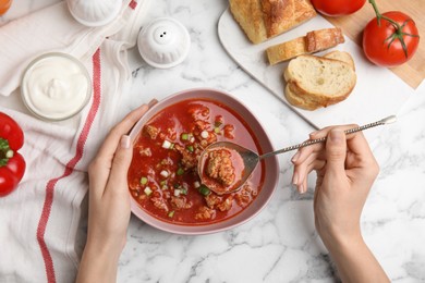 Woman with bowl of delicious stuffed pepper soup at white marble table, top view