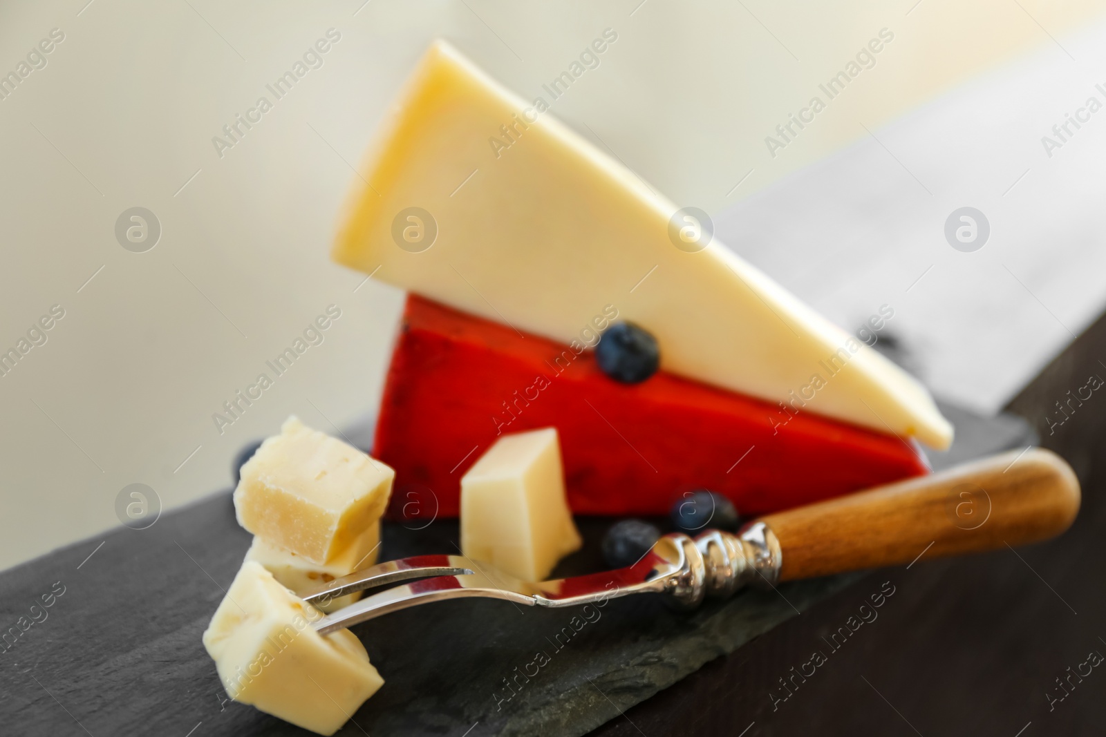 Photo of Fork with piece of delicious cheese on wooden railing, closeup