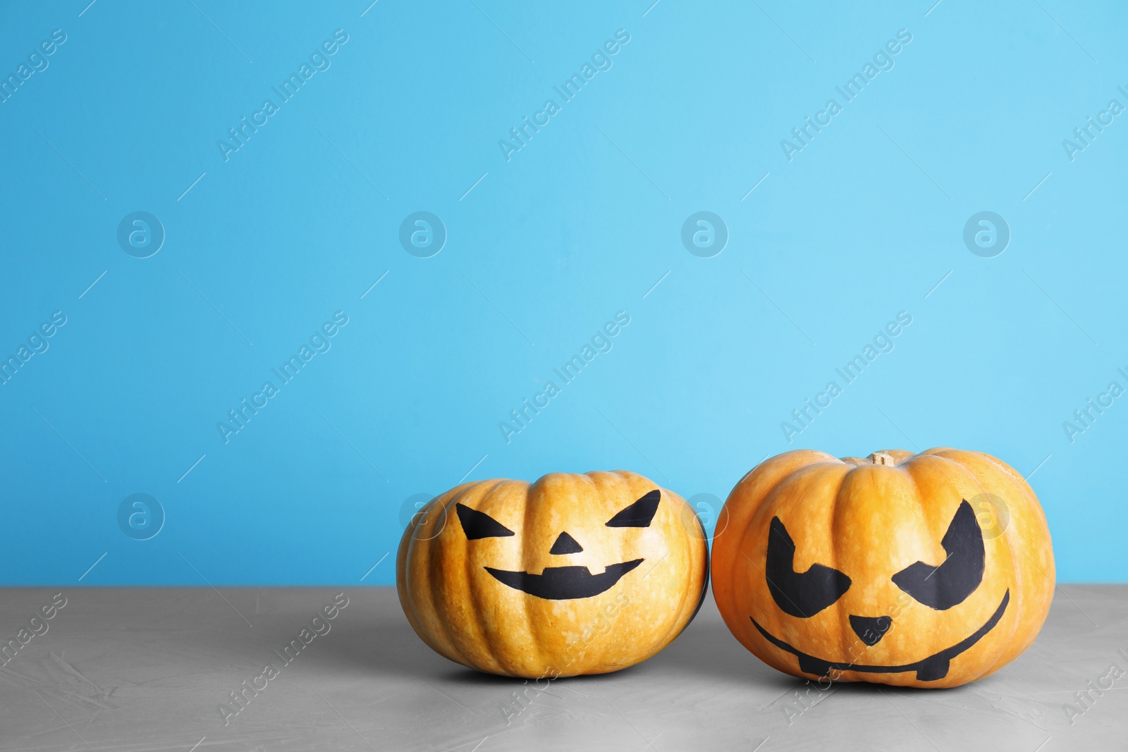 Photo of Pumpkins with scary faces on table against color background, space for text. Halloween decor