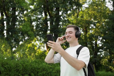 Photo of Smiling man in headphones using smartphone in park. Space for text