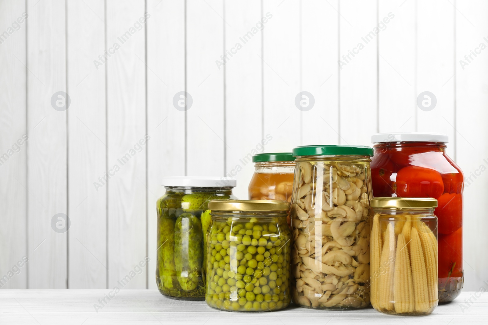 Photo of Glass jars with different pickled vegetables and mushrooms on white wooden background