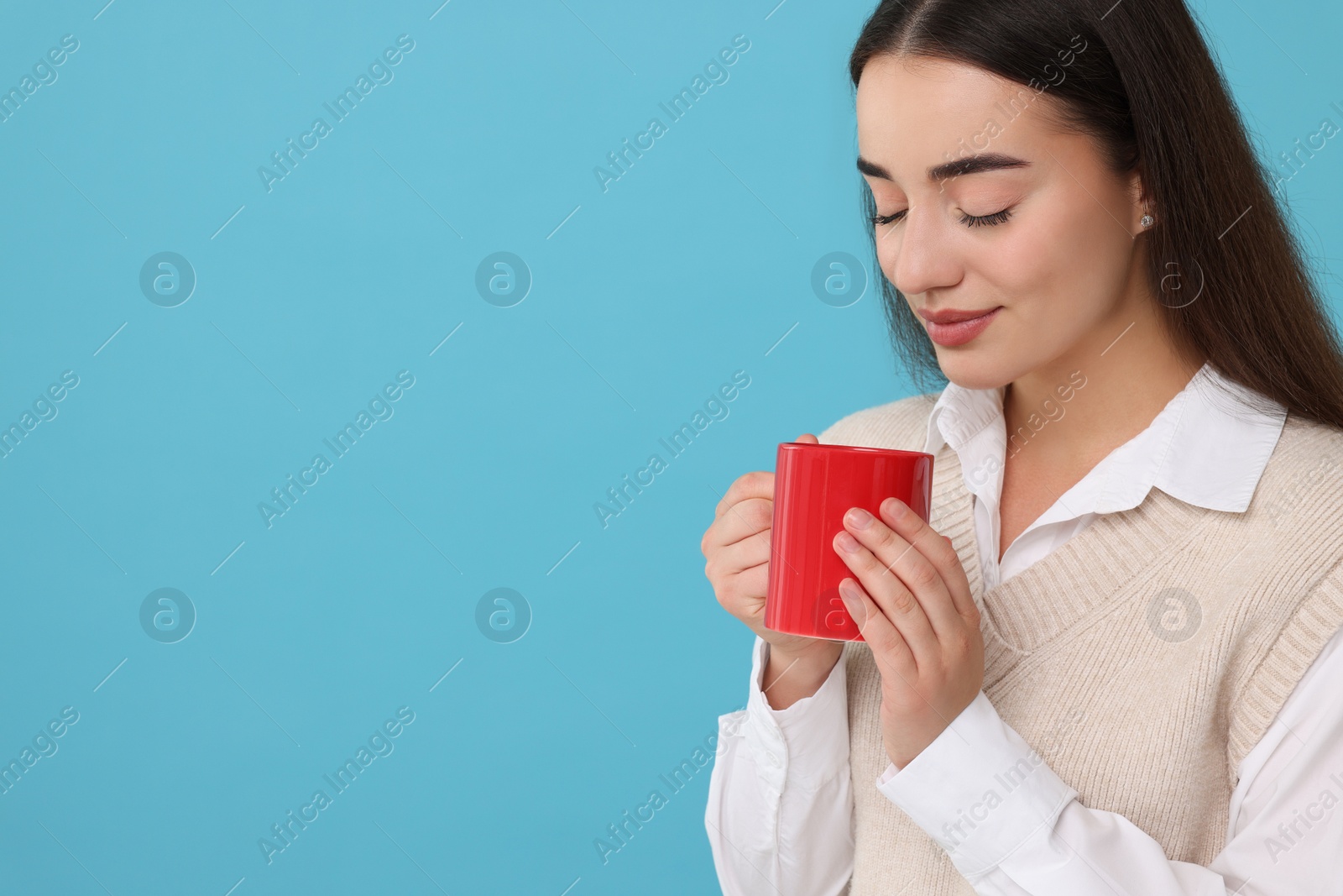 Photo of Beautiful young woman holding red ceramic mug on light blue background, space for text