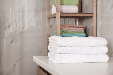 Stack of fresh towels on white table in bathroom. Space for text