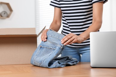 Photo of Young woman with just unpacked new jeans at wooden table indoors, closeup and space for text. Online shopping