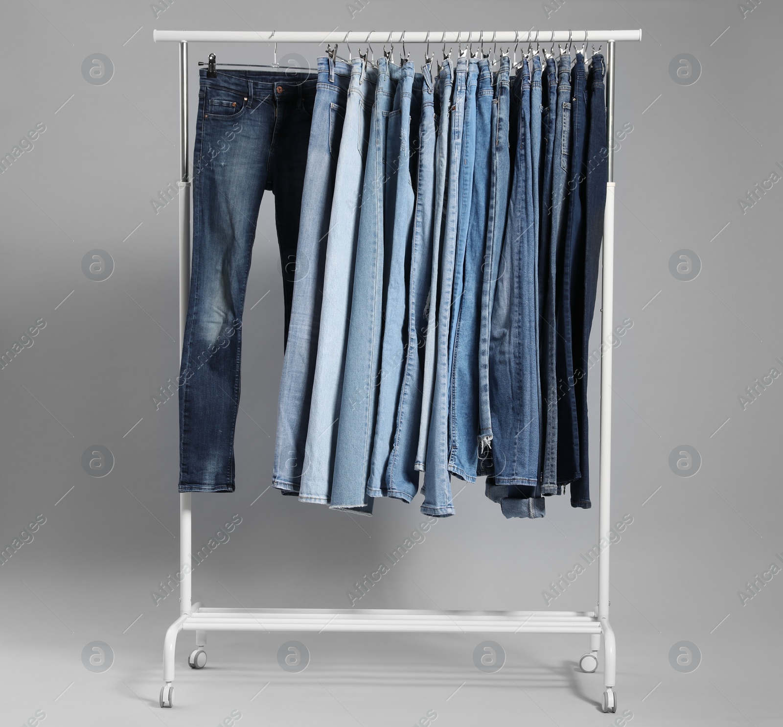 Photo of Rack with different jeans on grey background