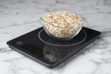 Photo of Digital kitchen scale with oat flakes on white marble table