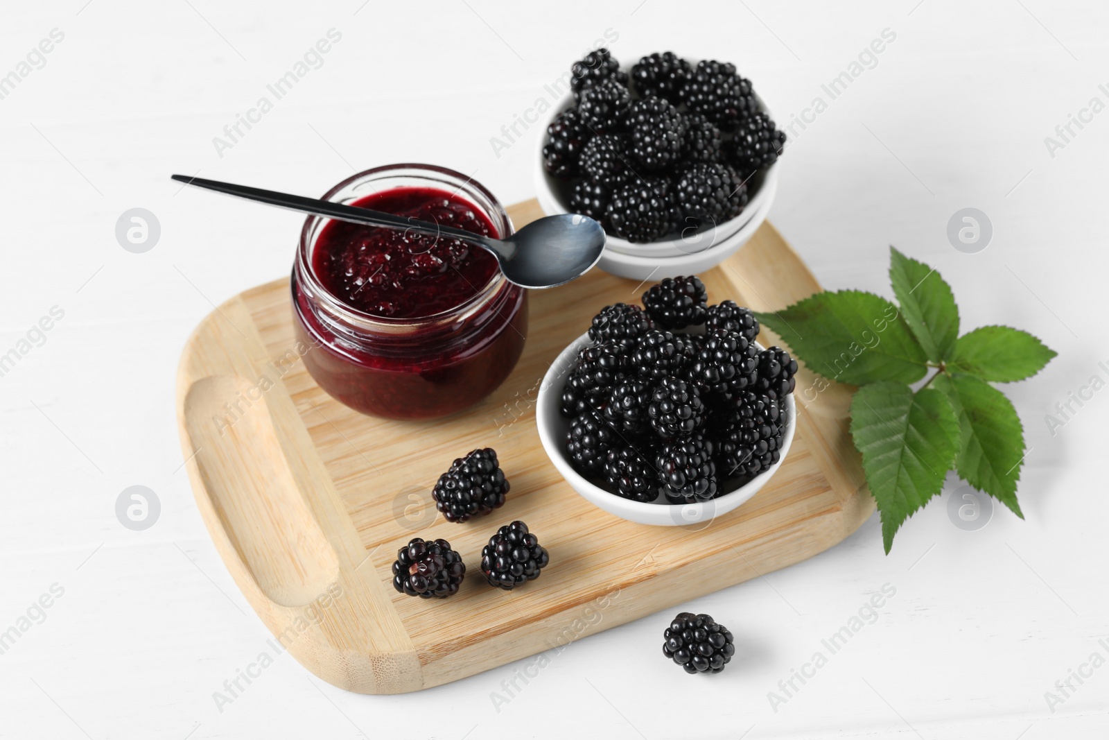 Photo of Fresh ripe blackberries, tasty jam and leaves on white table