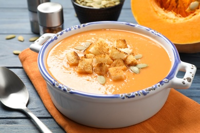 Photo of Tasty creamy pumpkin soup with croutons and seeds in bowl on blue wooden table