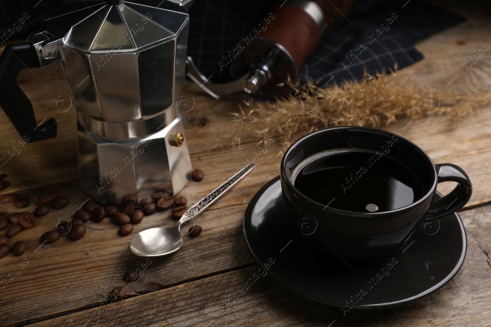 Photo of Cup of aromatic coffee, moka pot and scattered beans on wooden table